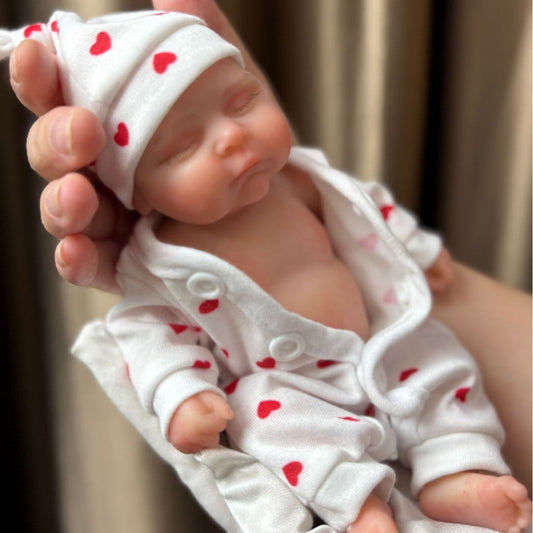 Mini bébé reborn fille Peaches en silicone yeux fermés 20cm vêtue d'une combinaison rouge à cœurs
