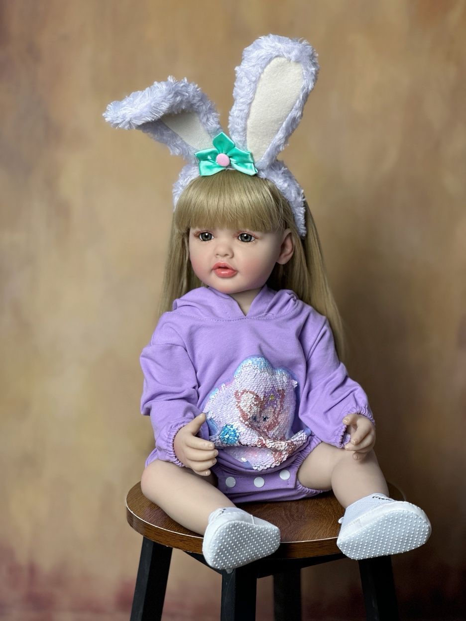 Bébé reborn de 55 cm yeux ouverts longs cheveux vêtue de vêtements violets et d'un serre-tête à oreilles de lapin - Betty